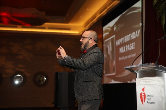 Auctioneer passionately speaks on stage beside American Heart Association podium.